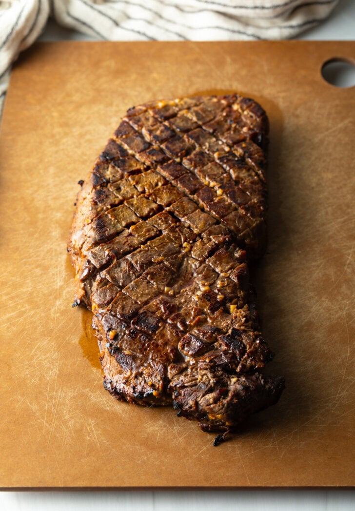 Seared London broil resting on a cutting board.