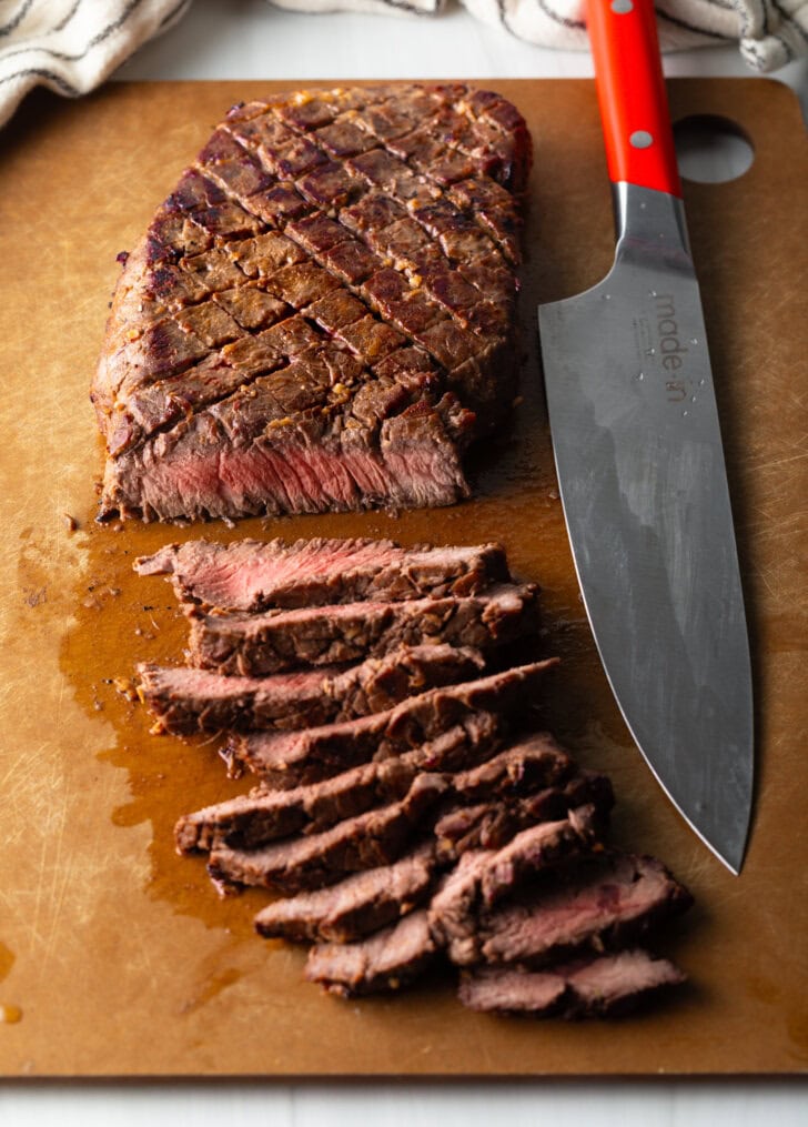 Top down view of london broil thinly sliced on a cutting board with large knife