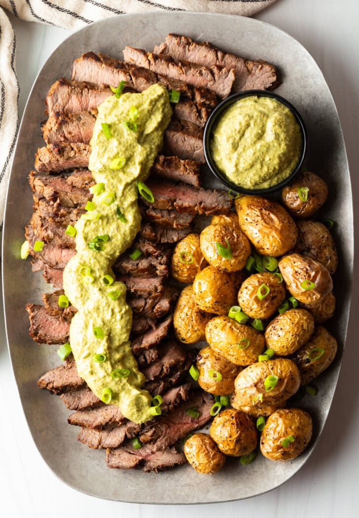 London broil sliced into thick strips, covered with rich green sauce and chopped scallions with baby potatoes on the side.