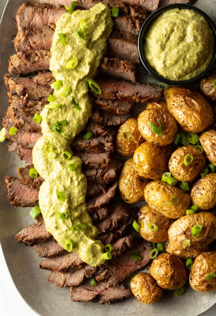London broil sliced into thick strips, covered with rich green sauce and chopped scallions with baby potatoes on the side.