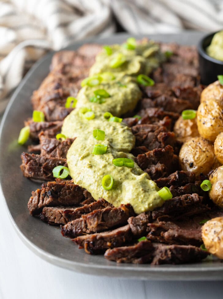 London broil sliced into thick strips, covered with rich green sauce and chopped scallions with baby potatoes on the side.