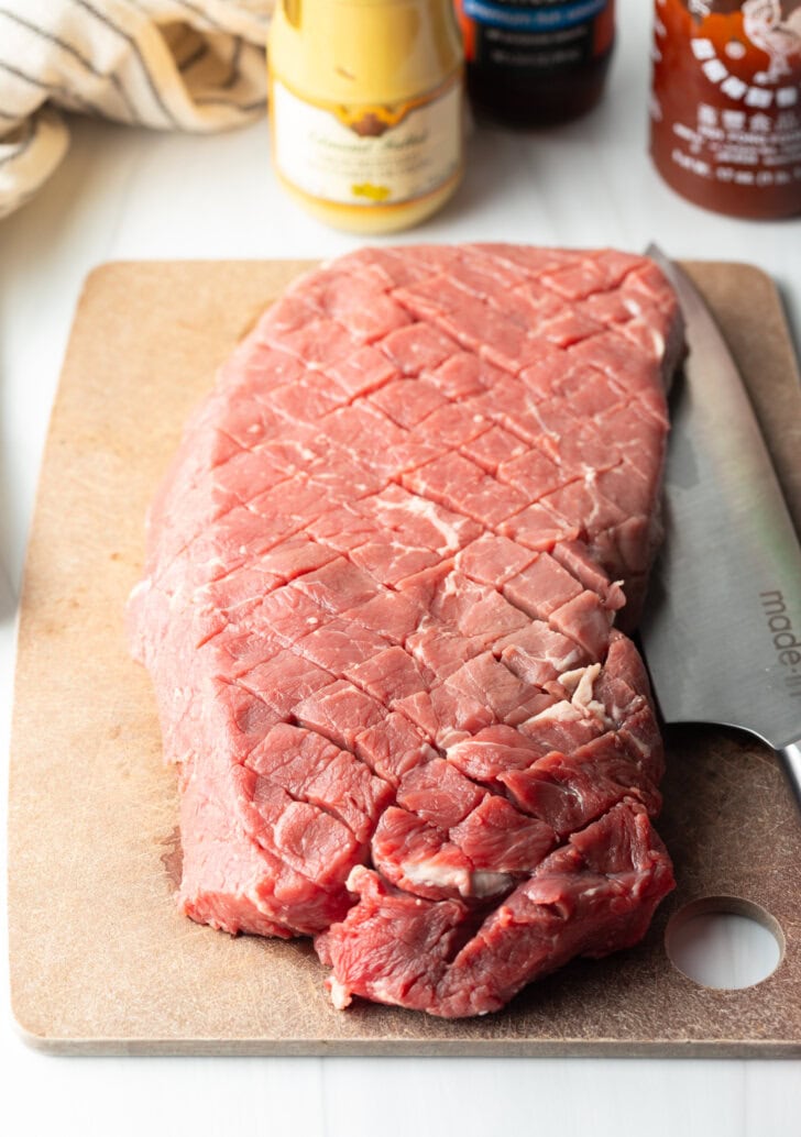 Large section of London broil on a cutting board, with the top scored in a criss-cross diagonal pattern.