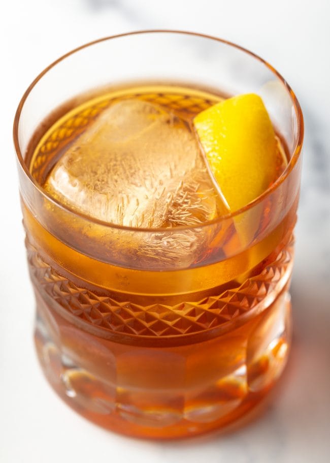 Manhattan Cocktail | ASpicyPerspective.com #holiday #cocktails Manhattan drink in a rocks glass garnished with a lemon rind.