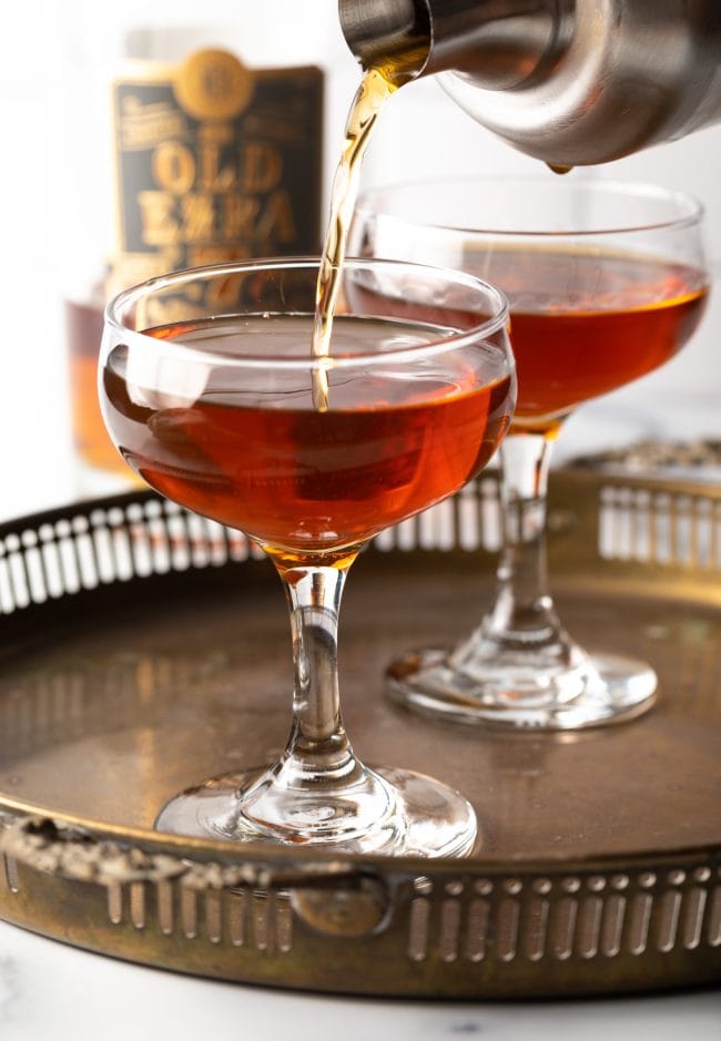Perfect Manhattan Recipe being poured from a shaker into a coupe glass.