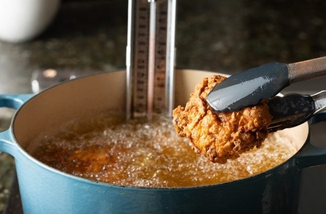 Tongs taking out a piece of fried chicken from the pot of oil.
