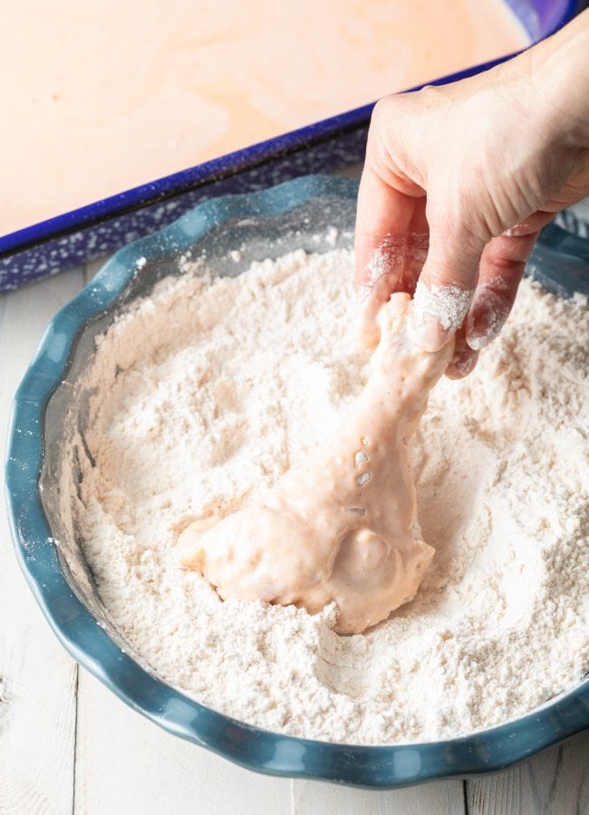 Hand dipping chicken legs in flour to fry.