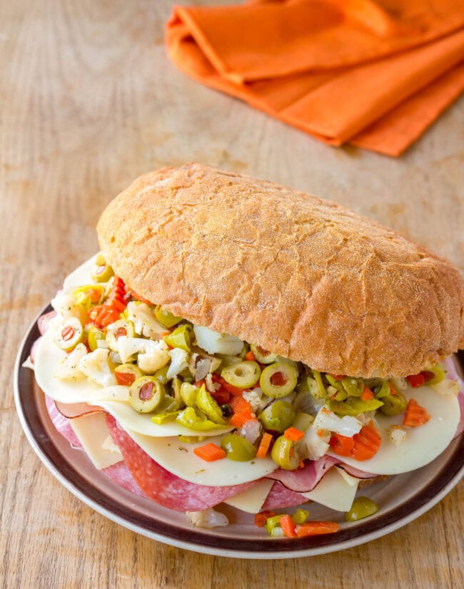 New Orleans Muffuletta #ASpicyPerspective #NewOrleans #Sandwich #Muffuletta #MuffulettaSandwich #MuffulettaRecipe #OliveSalad New Orleans Muffuletta on plate, loaded with meat, cheese and olive salad.