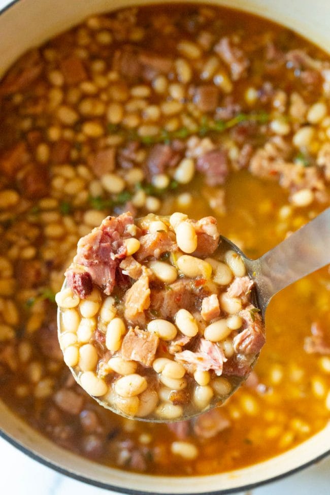 Navy Bean Soup #ASpicyPerspective #HamAndBeanSoup #NavyBeans #HamAndBeans #NavyBeanSoup #BeanSoup #Soup Ladle full of soup above a full pot fresh off the stove