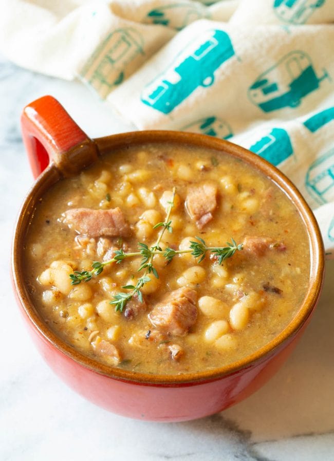 Navy Beans #ASpicyPerspective #HamAndBeanSoup #NavyBeans #HamAndBeans #NavyBeanSoup #BeanSoup #Soup Red bowl with a handle filled with navy bean soup with ham.