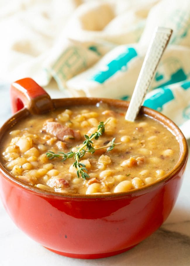 Navy Beans #ASpicyPerspective #HamAndBeanSoup #NavyBeans #HamAndBeans #NavyBeanSoup #BeanSoup #Soup Single serving of navy bean soup with beans in a red bowl with a handle and a metal spoon sticking out