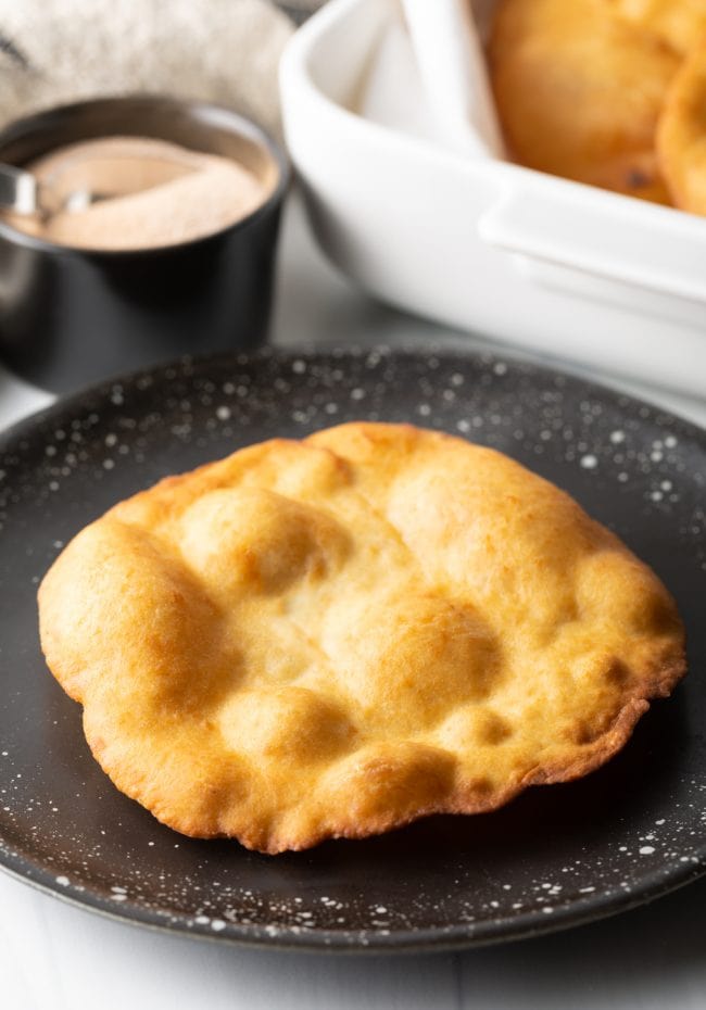 Crispy fry bread on a black plate.