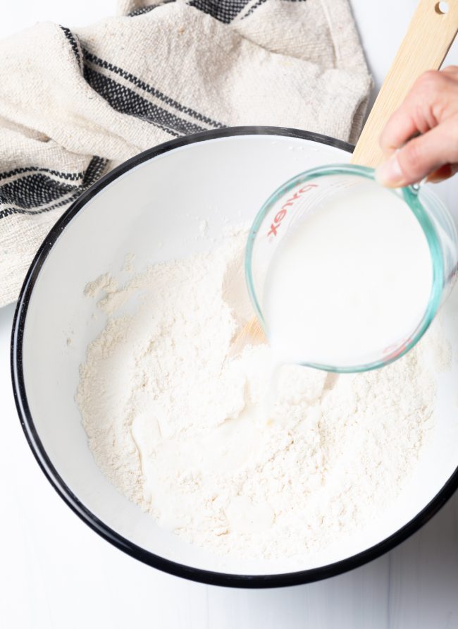 Hand pouring wet ingredients into the mixing bowl to make the dough.