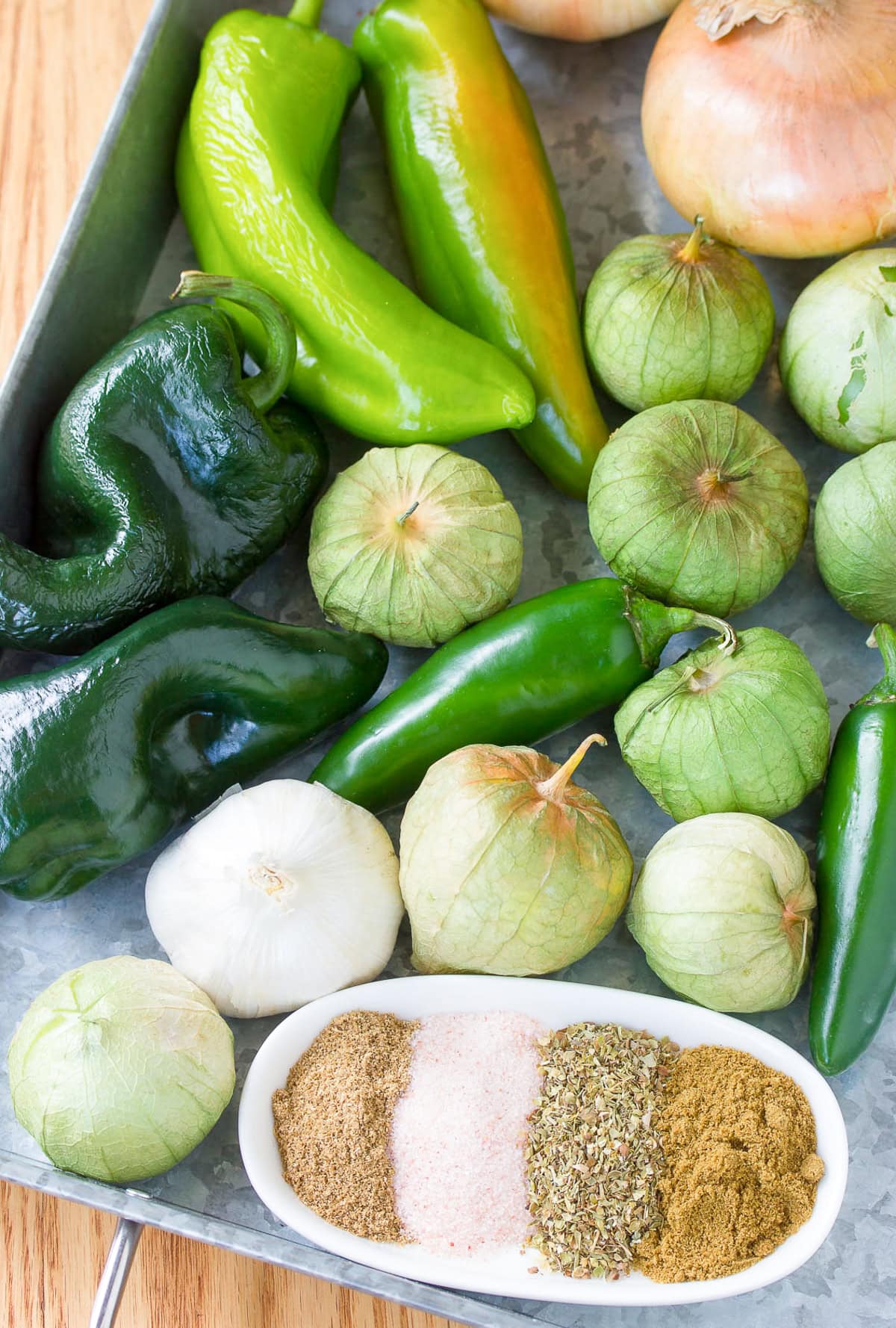 Peppers, tomatillos, onions and spices on a sheet pan.