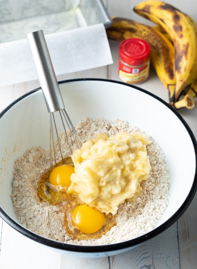 Flour and oats with eggs and smashed banana in a mixing bowl.