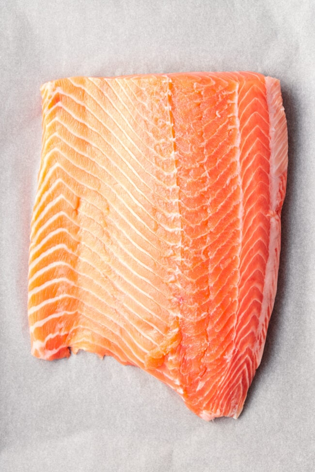 Salmon #ASpicyPerspective #Salmon #BakedSalmon #OvenBakedSalmon #SalmonRecipe #BakedSalmonRecipe #OvenBakedSalmonRecipe #HowtoBakeSalmon #ParmesanCrust #Fish #Dinner #MainDish Parmesan Crusted Salmon - Raw wild salmon fillet on parchment paper.