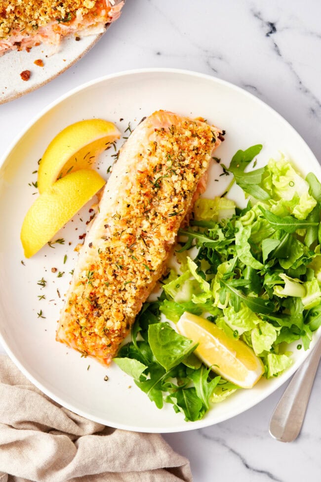 Salmon Recipe #ASpicyPerspective #Salmon #BakedSalmon #OvenBakedSalmon #SalmonRecipe #BakedSalmonRecipe #OvenBakedSalmonRecipe #HowtoBakeSalmon #ParmesanCrust #Fish #Dinner #MainDish Oven baked salmon with a parmesan herb crust on a baking sheet with a spatula on the side.