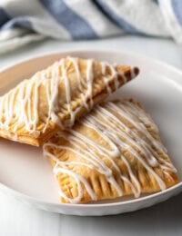 Two homemade peach pop tarts resting against each other on a white plate.