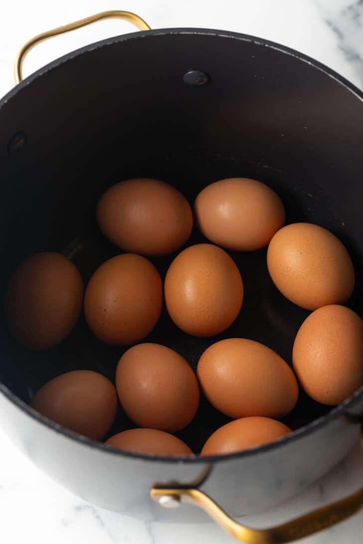 A dozen brown eggs in a large black pot.