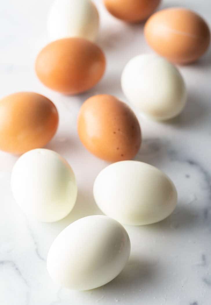 Top down view, four peeled hard boiled eggs and three brown unpeeled eggs.