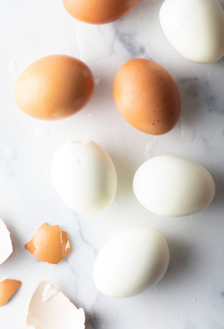 Top down view, four peeled hard boiled eggs and three brown unpeeled eggs.