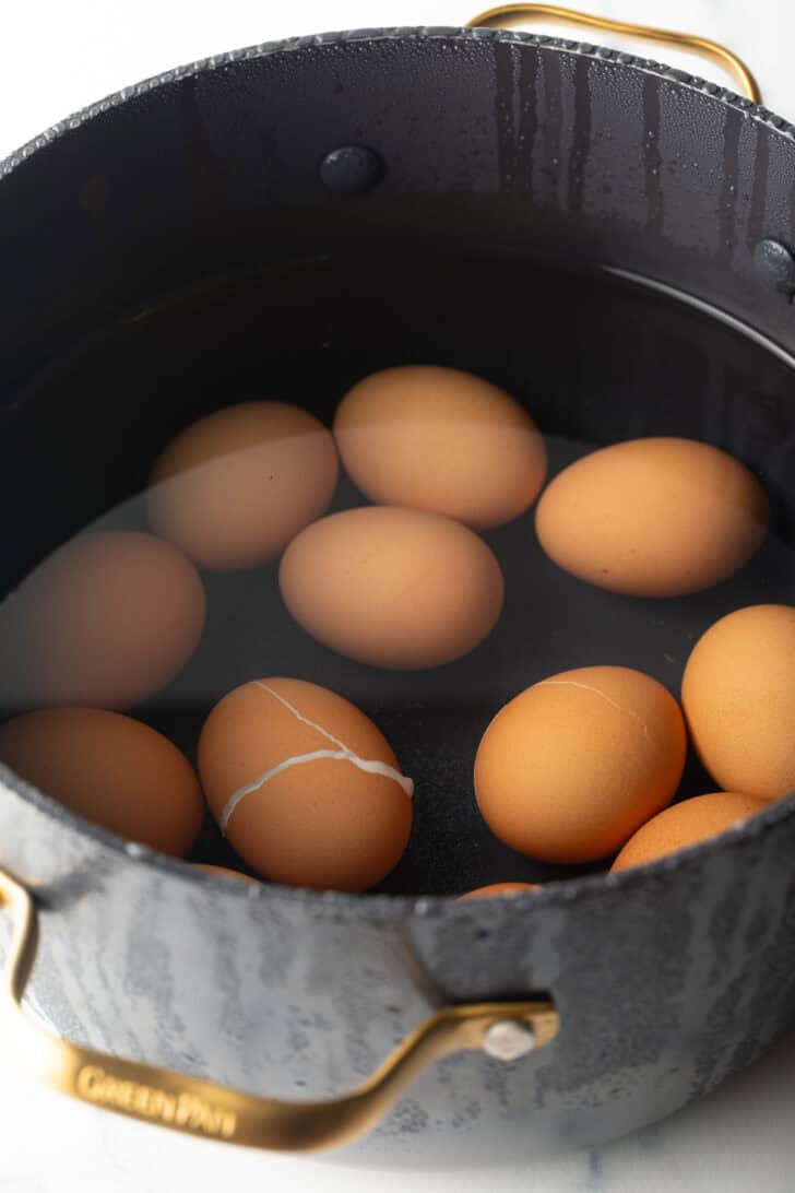 A dozen brown eggs covered in water in a large black pot.