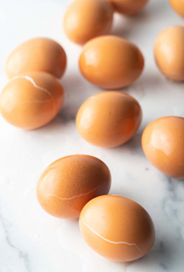 A dozen hard boiled brown eggs on a marble background.