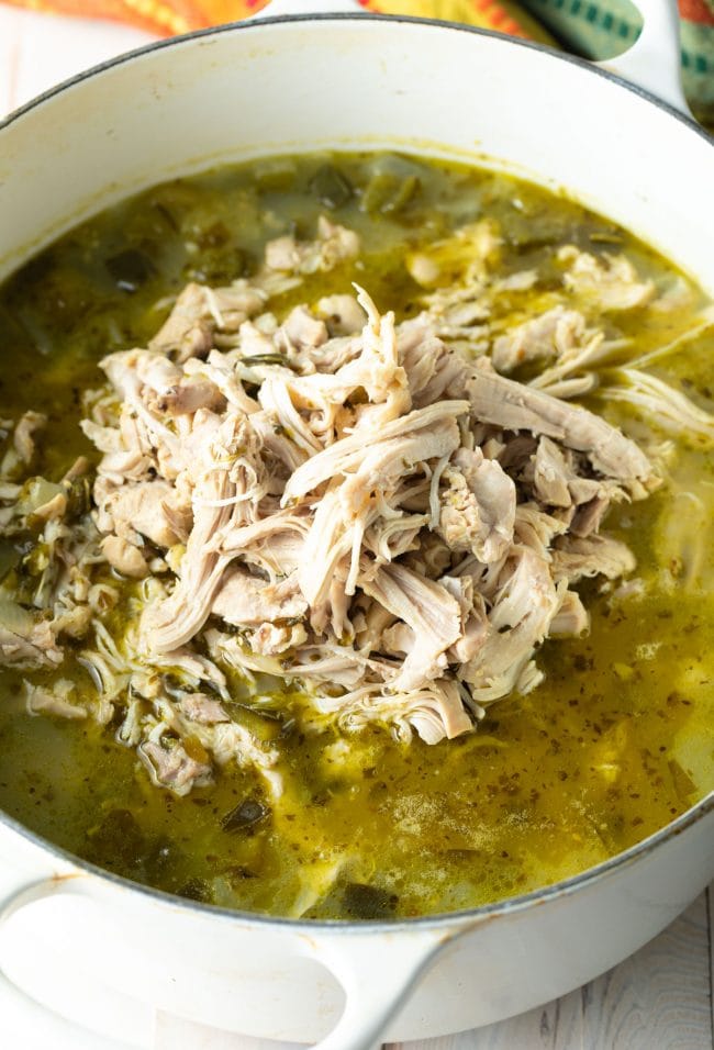 Shredded chicken being added back into the Pozole Verde pot.