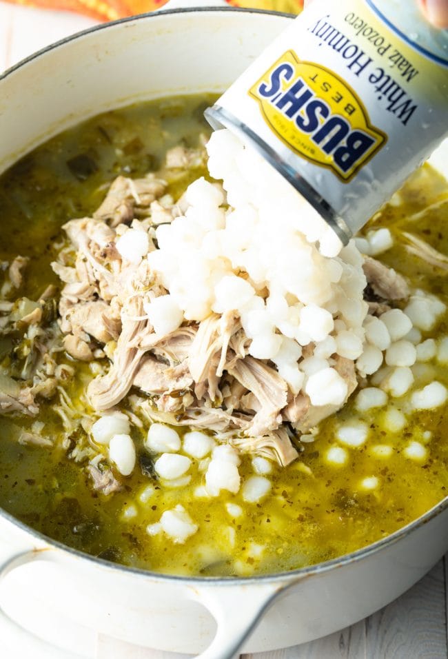 Can of white hominy being added to the pot of pozole verde.