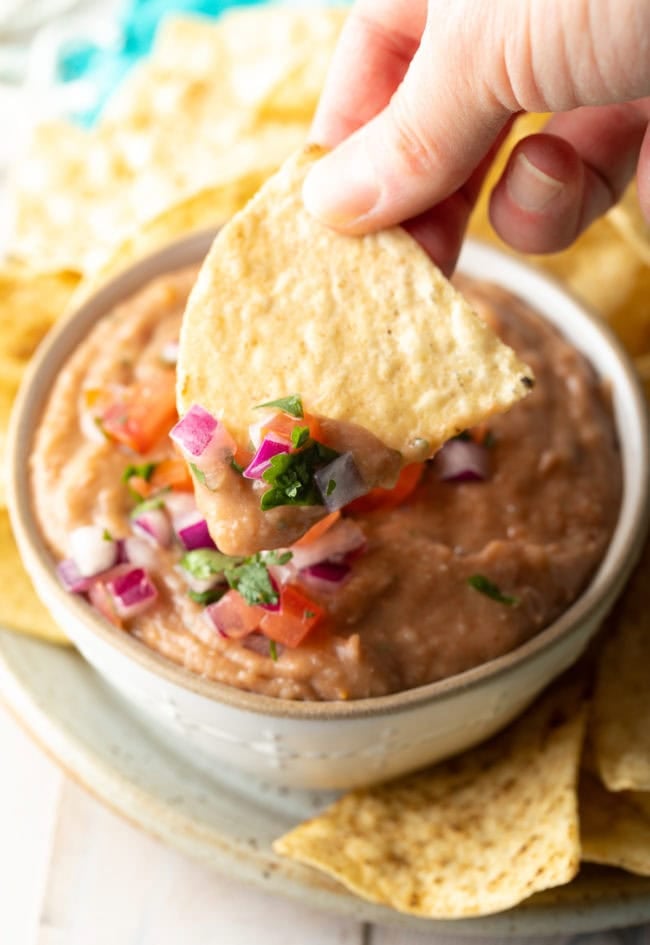 Hand holding a tortilla chip and dipping it into the bean dip.