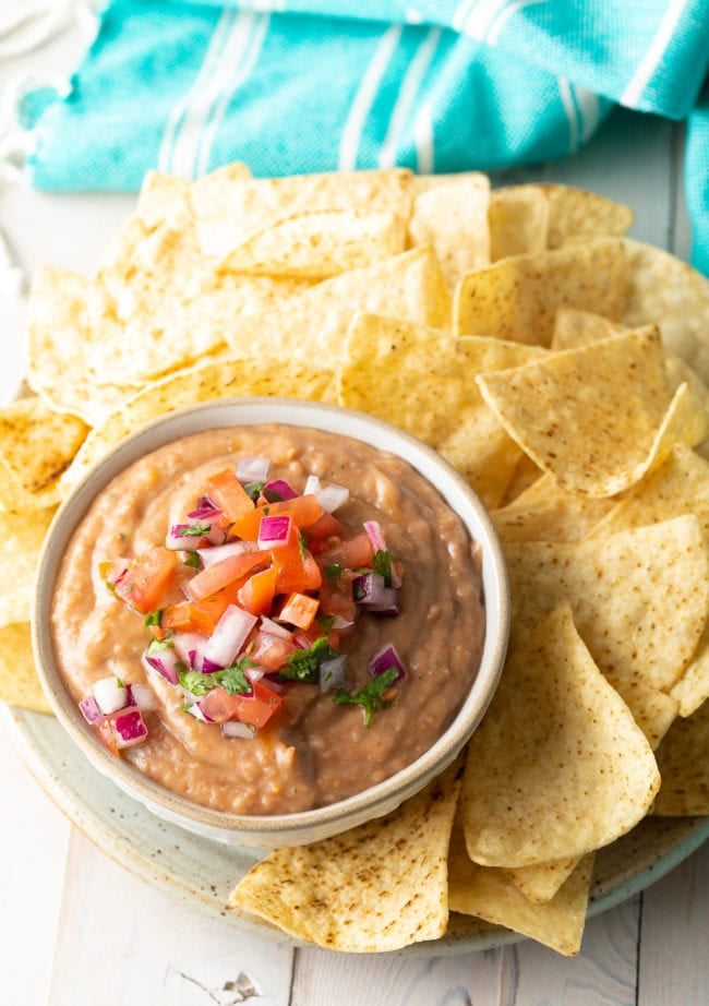 Pinto bean dip served in a bowl with pico de gallo on top next to a plate of tortilla chips.