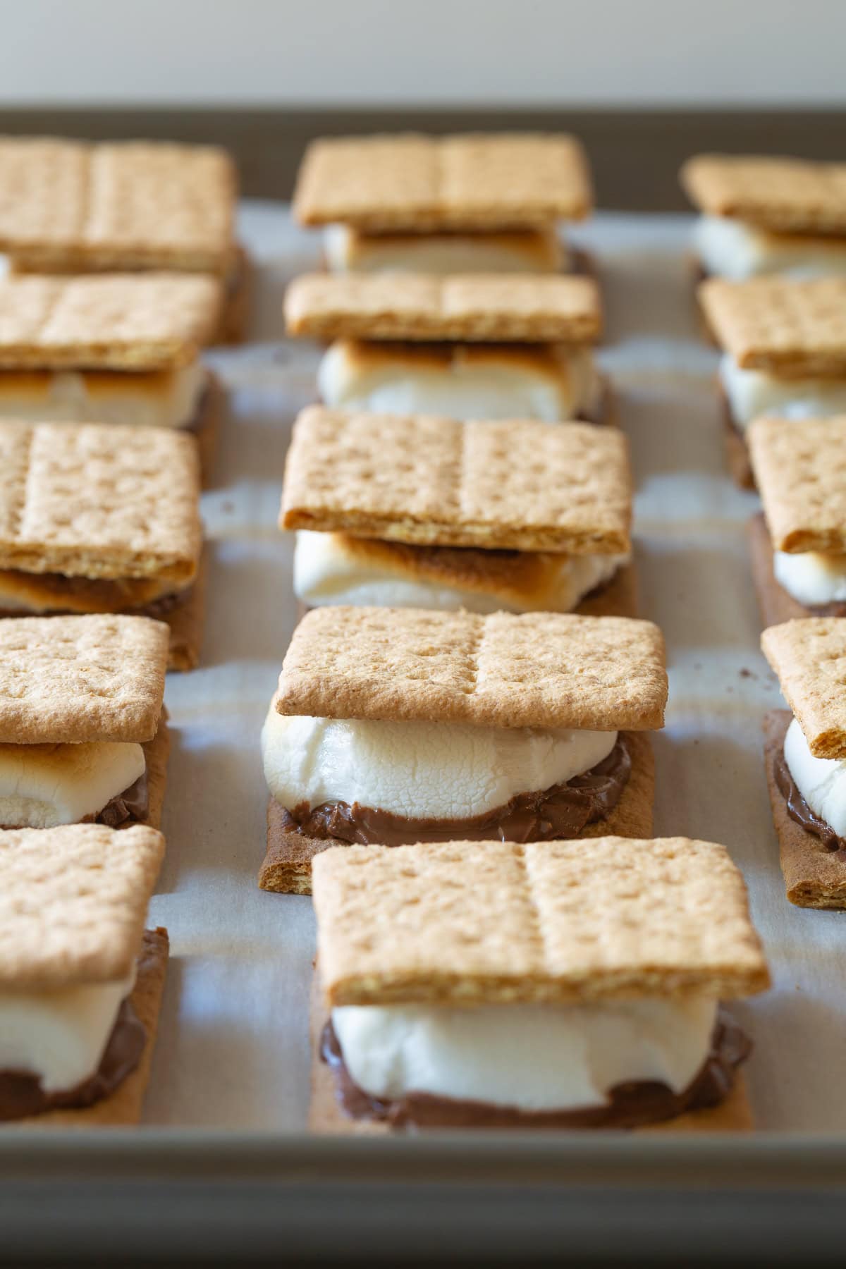 Baked smores lined up on a baking sheet lined with parchment paper.