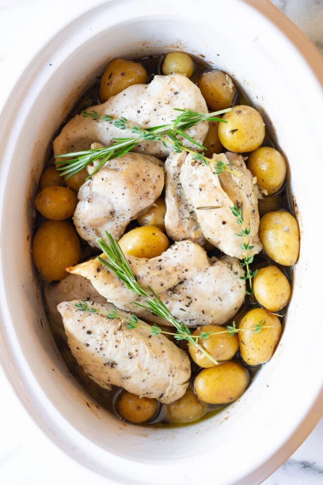 Slow cooker garlic butter chicken in the crockpot with herbs on top.