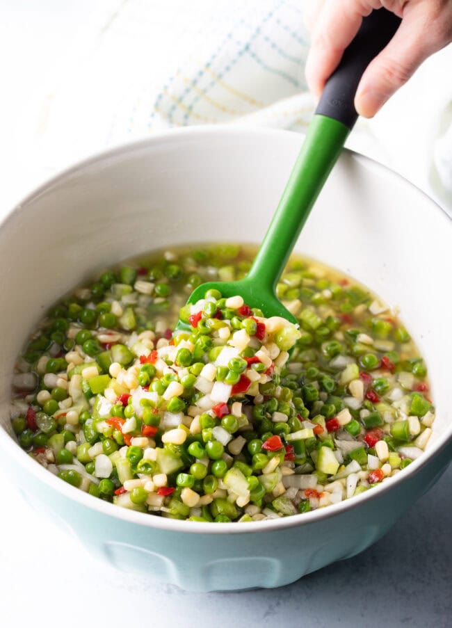 Green spatula stirring veggies in a white bowl.