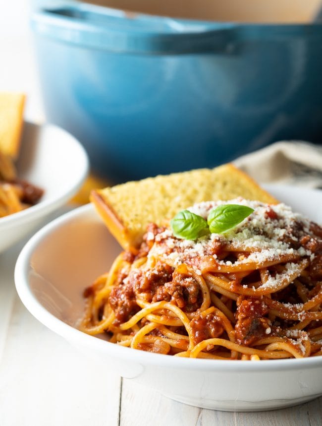 Spaghetti with meat sauce in a bowl served with garlic bread.