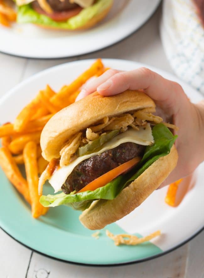 Spicy Burger Recipe in hand with plate of french fries in the background.