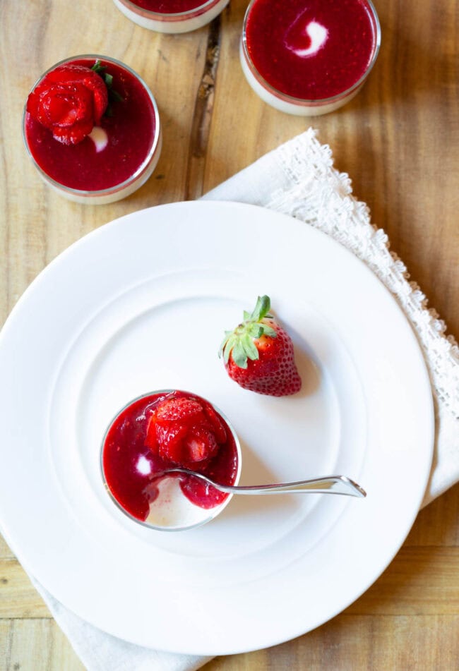 Top down view glass dish with silky swedish cream topped with berry compote and strawberry rose. A second whole strawberry is next to the dish.