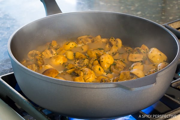 Mushrooms with seasonings sautéing in a pan on the stove.