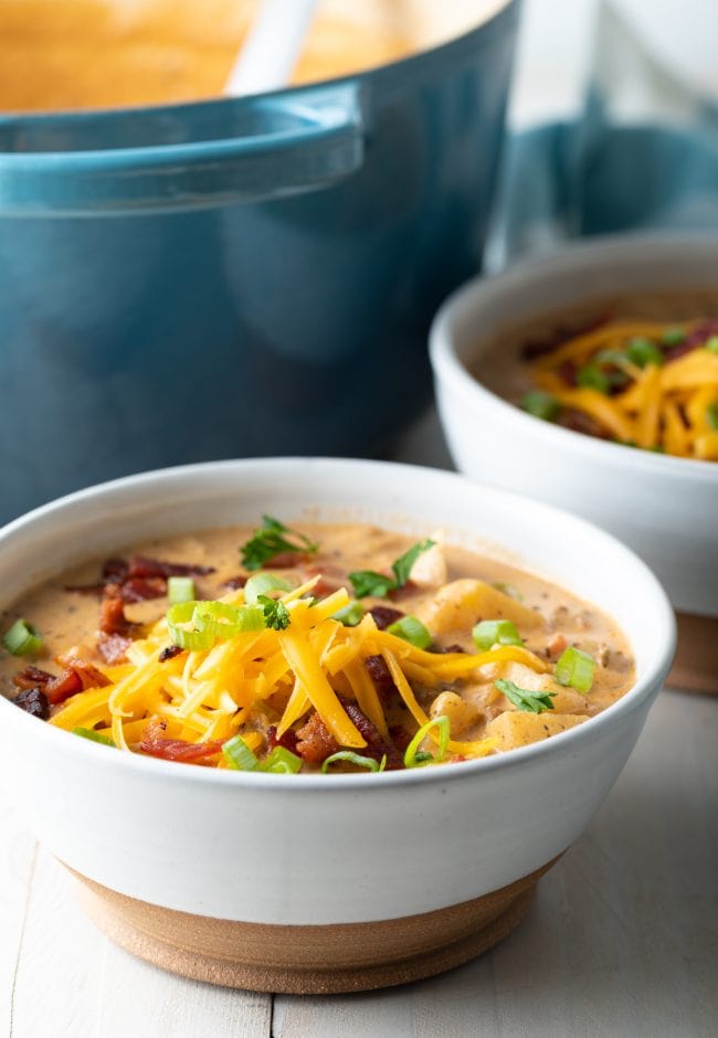 Two bowls of cheeseburger soup topped with bacon bits, cheese, and green onions.