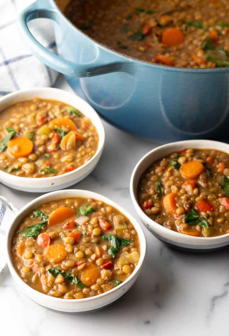 3 white bowls of lentil soup with carrots and kale.