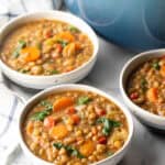 3 white bowls of lentil soup with carrots and kale.