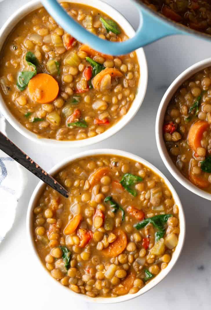 3 white bowls of traditional lentil soup with carrots and kale.