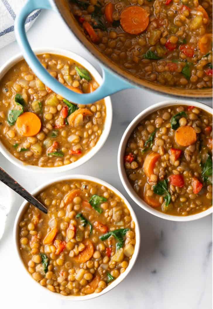 3 white bowls of lentil soup with carrots and kale.