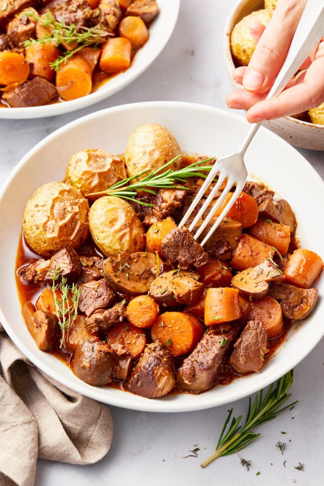 venison-stew.jpg Venison Stew Recipe in a white bowl with a side of potatoes.