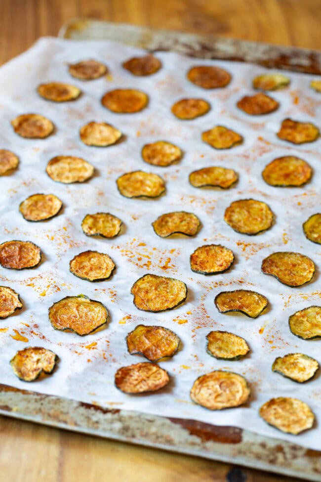 Baked Zucchini Chips #ASpicyPerspective #Healthy #Paleo #Vegan #GlutenFree #Vegetarian #ZucchiniChips #OvenRoasted Oven Baked Zucchini Chips on cookie sheet with parchment paper